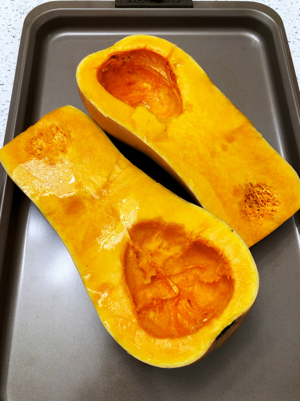 Butternut squash cut lengthwise with seeds removed on baking tray