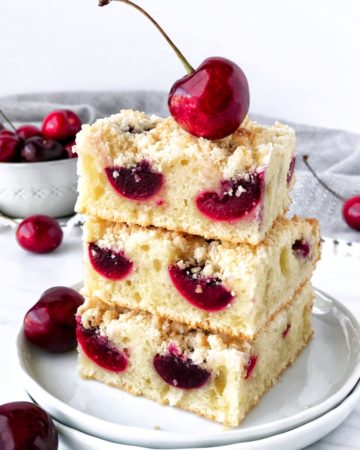 3 bars of cherry fruit cake on a plate. Cherries in a bowl in a background