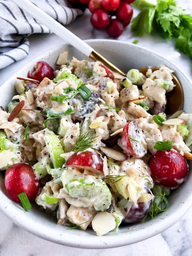 chicken salad with grapes, almonds and celery in a grey bowl, napkin in the left bottom corner, fresh grapes and celery on top of the picture