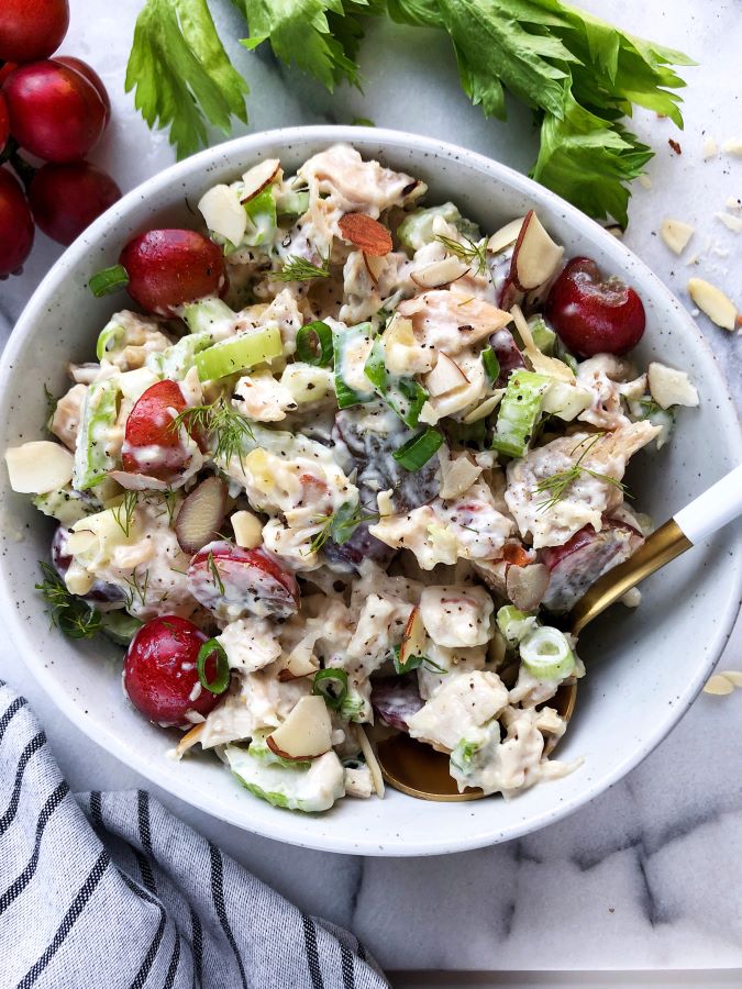 chicken salad with grapes, almonds and celery in a grey bowl, napkin in the left bottom corner, fresh grapes and celery on top of the picture