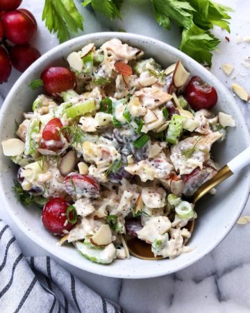 chicken salad with grapes, almonds and celery in a grey bowl, napkin in the left bottom corner, fresh grapes and celery on top of the picture