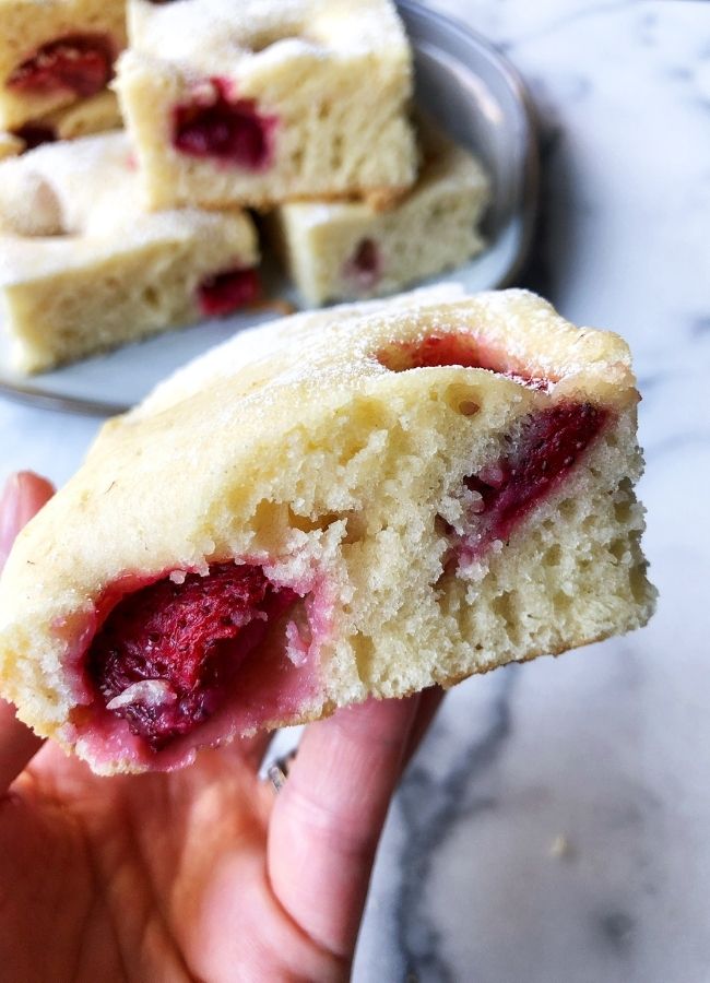 A hand holding strawberry bubble cake square, more cake on a plate in a background 