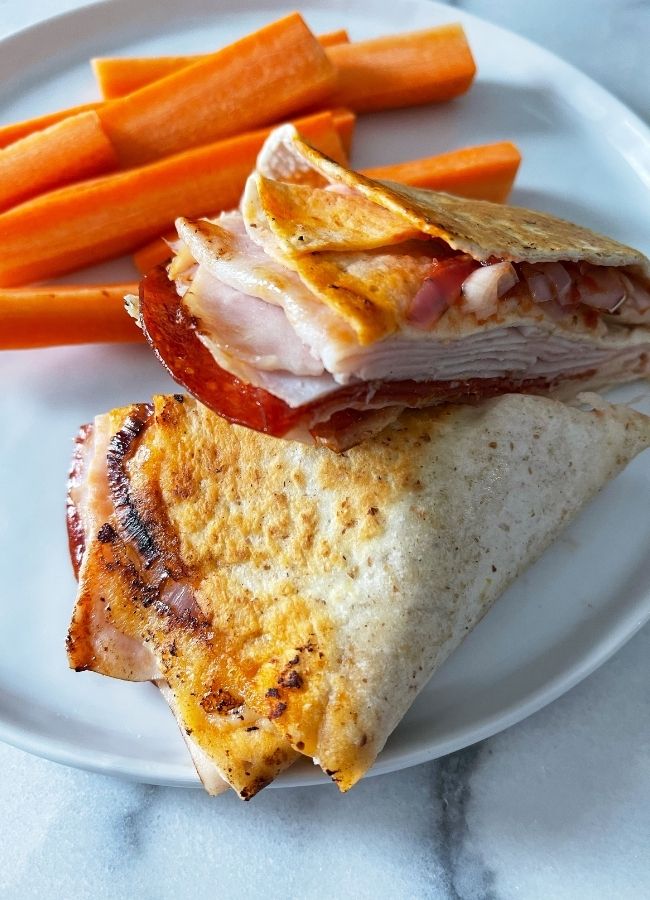 pizza style tortilla wrap cut in half on a white plate with fresh carrot sticks